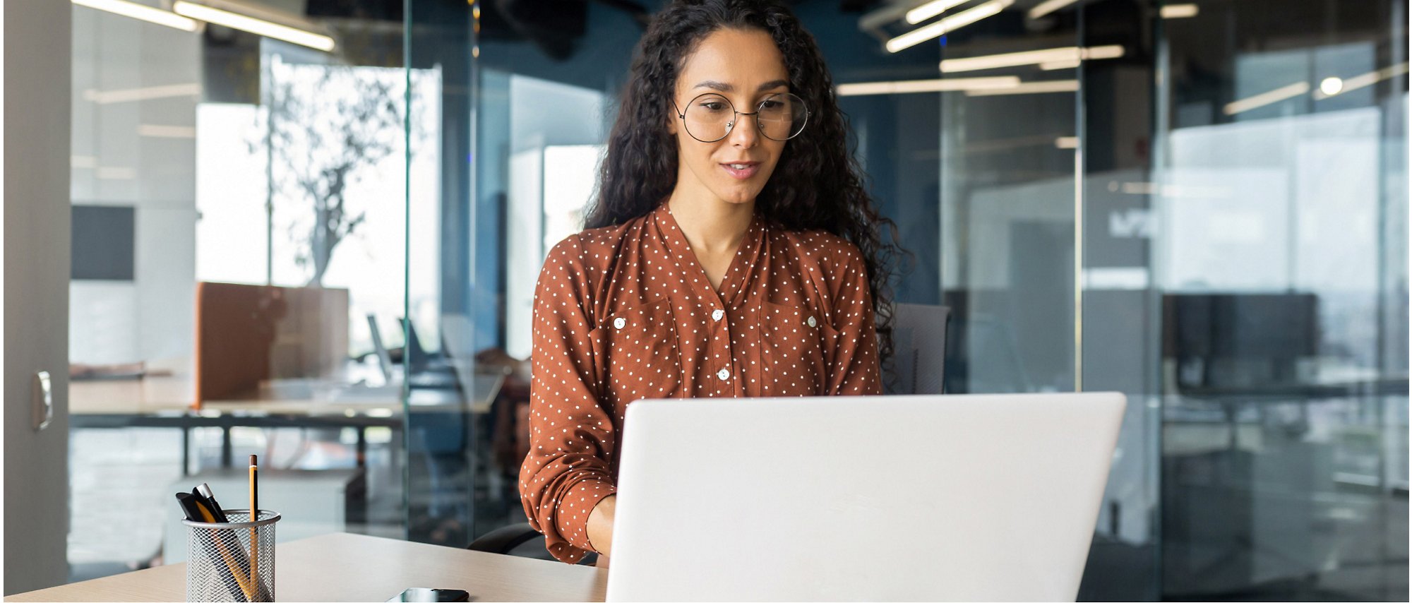 A person in a polka dot shirt working on a laptop in a modern office environment.