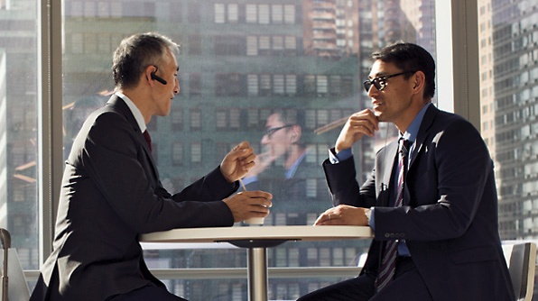 Two men in business suits are seated at a round table, engaged in conversation. 