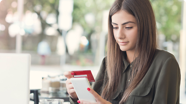 A woman holding a smartphone in one hand and a credit card in the other, while seated at a table.