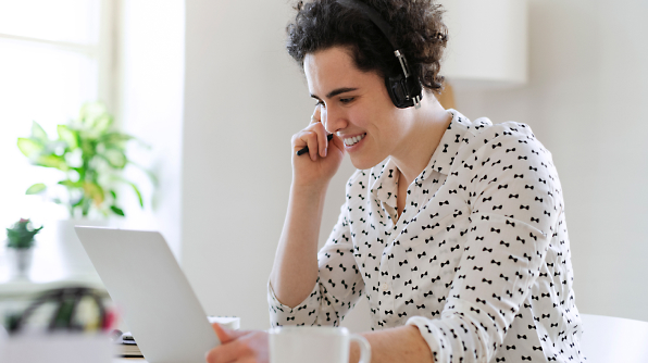 A Person is wearing headphones, smiling and looking at a laptop screen in a bright room.