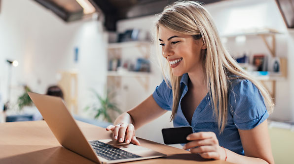 A woman is smiling while using a laptop and holding a credit card in her hand. 