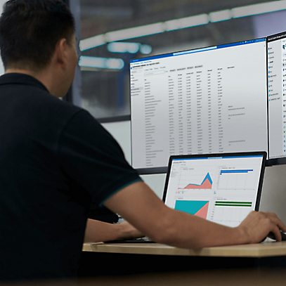 A person sitting and working on laptop looking at dashboard with two additional monitors on the desk