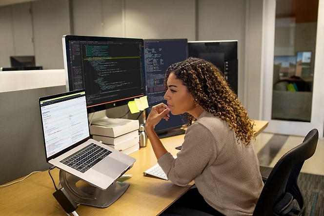 En kvinde, der tænker, med hænderne på sit ansigt, mens hun kigger på den bærbare computer