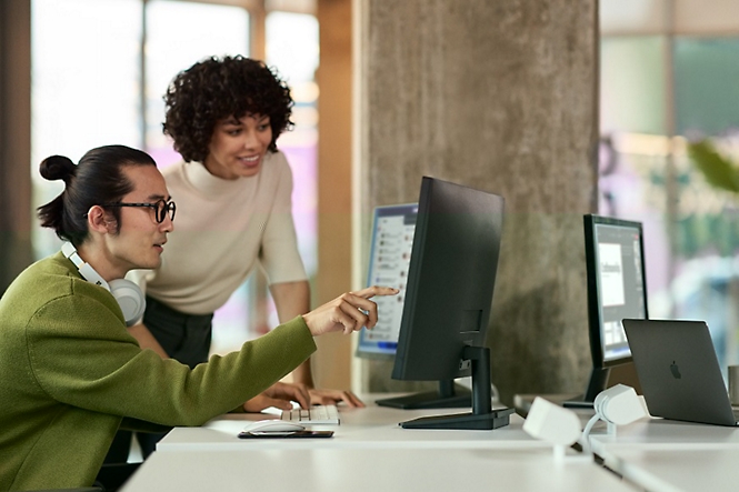 Two people looking in the desktop and one person pointing at screen with finger