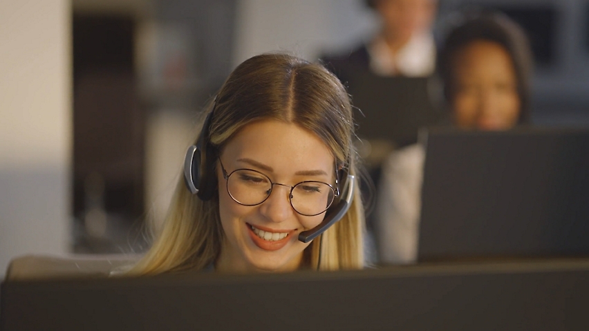 A woman sitting in office infront of her desktop and talking while wearing headset