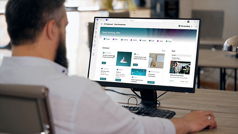 Man at a desk viewing a personalized dashboard on a computer screen, featuring news and documents.