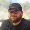 A smiling man in a ballcap and glasses.