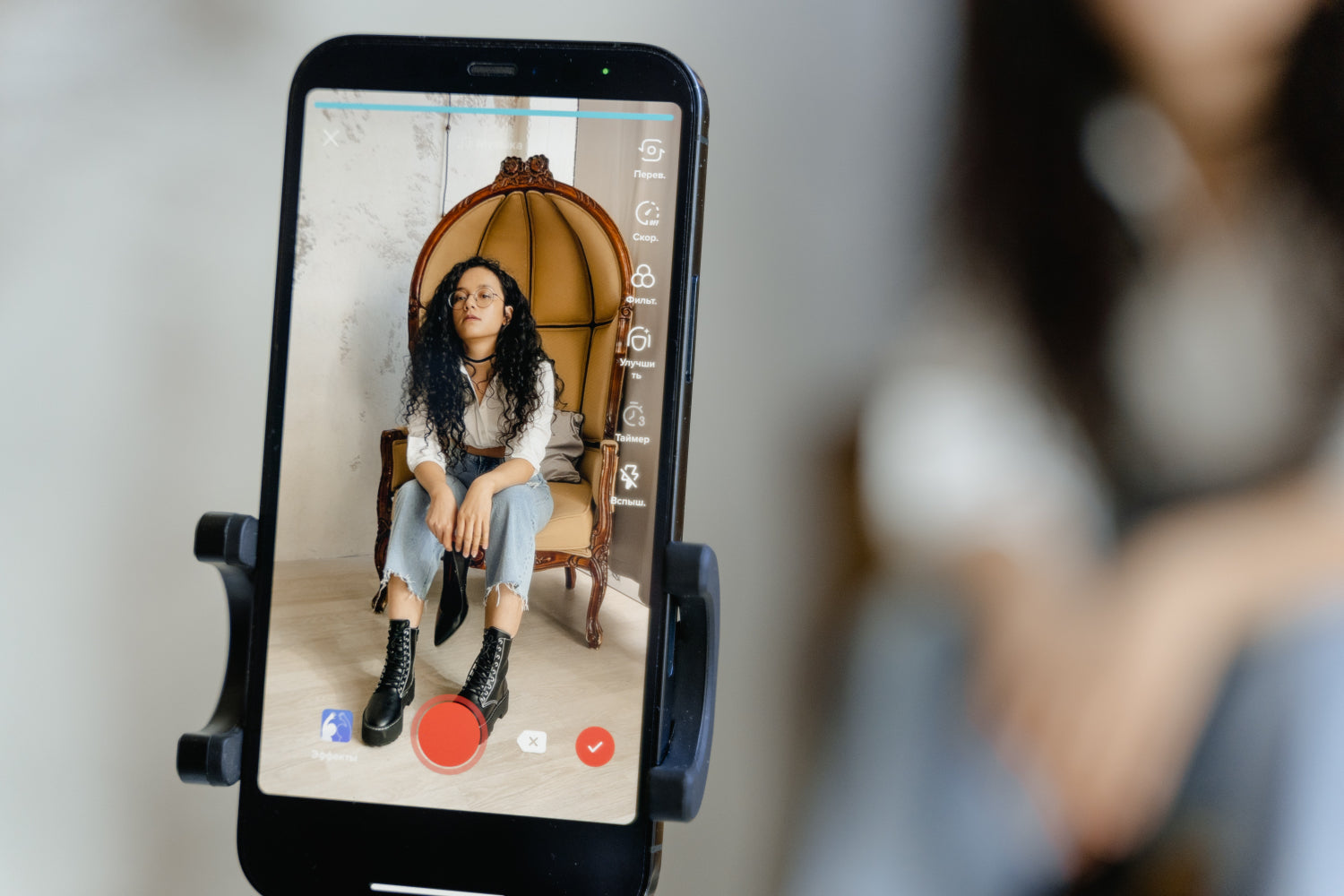 A phone screen is in the foreground showing a live video recording of a young person in a chair