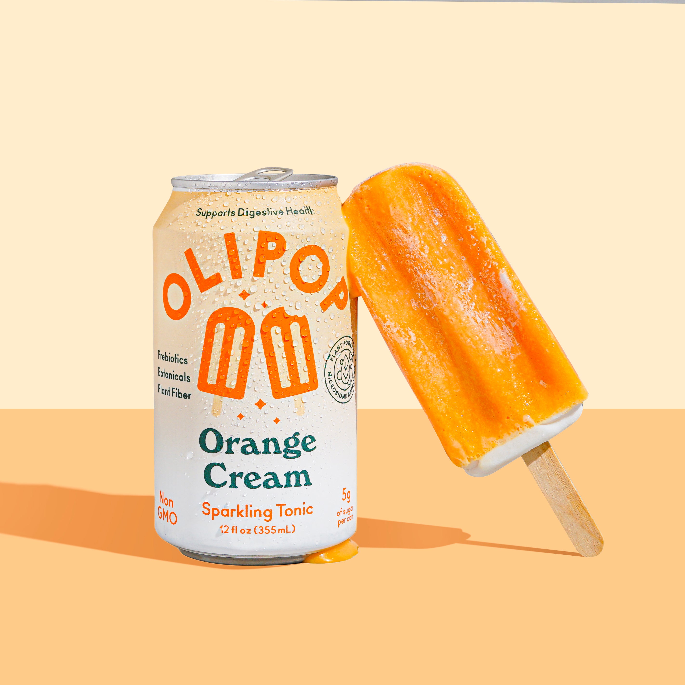 A can of orange creamsicle olipop with a popsicle leaning against it, backdropped by light orange background. 