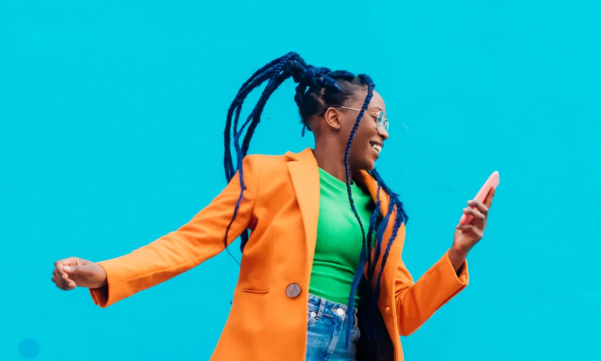 Woman jumping in front of a bright blue wall while looking at her smartphone