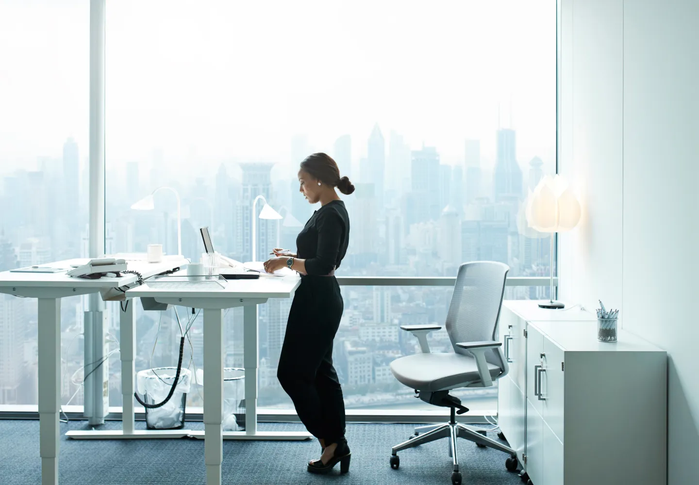 Woman standing at a desk and making notes in front of a large window overlooking a city