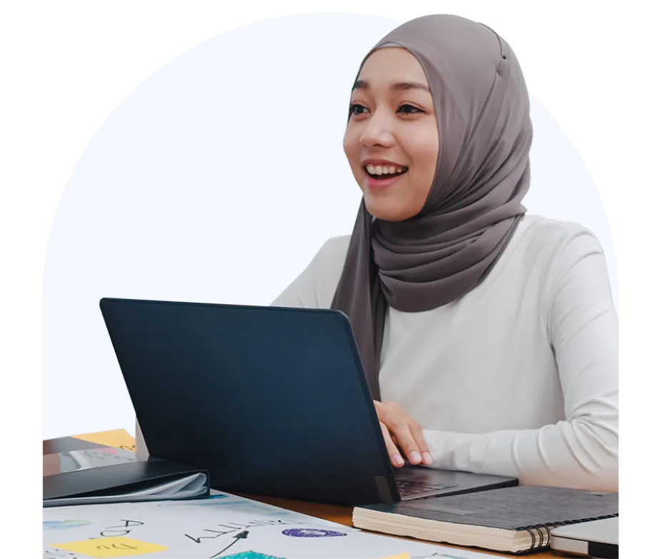 A woman sits at a table in front of a laptop smiling 