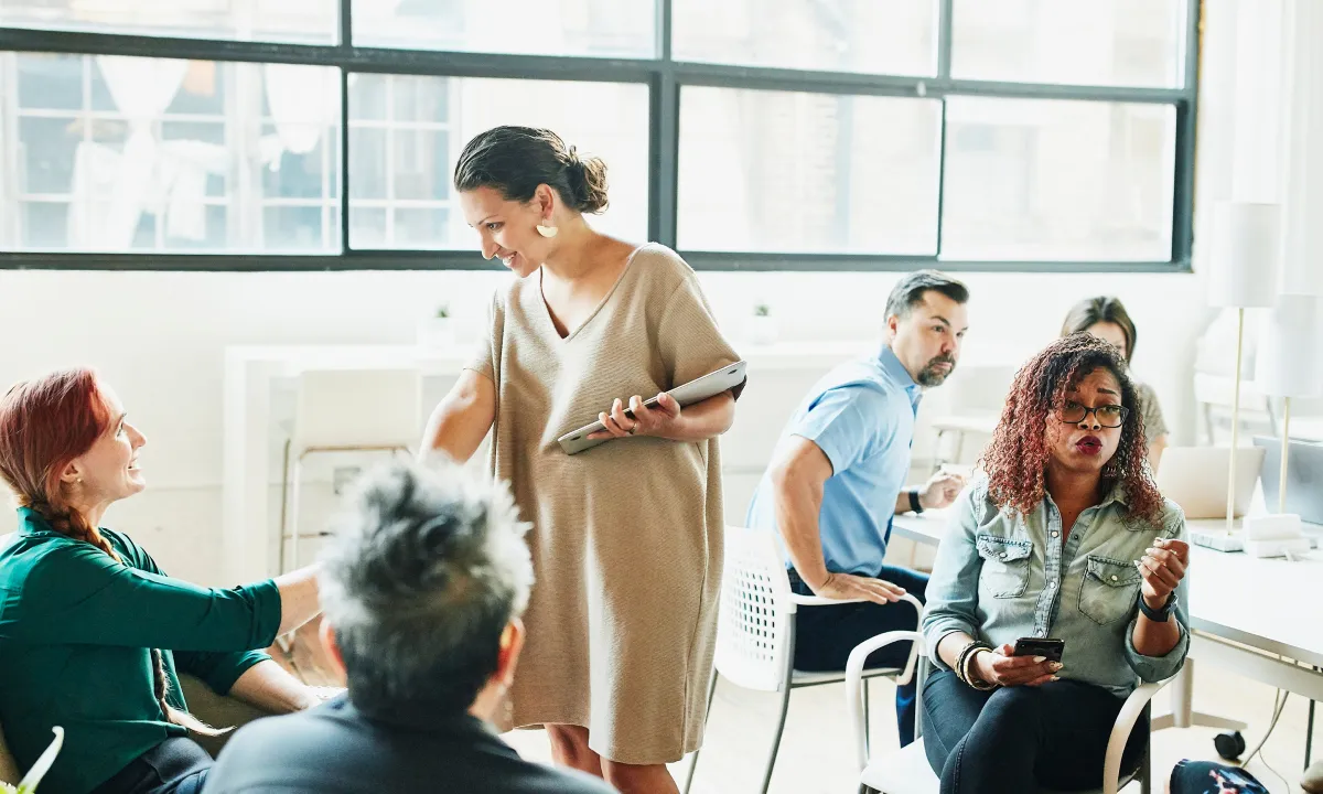 Colleagues in an open meeting space. One woman standing is shaking hands with a seated woman.