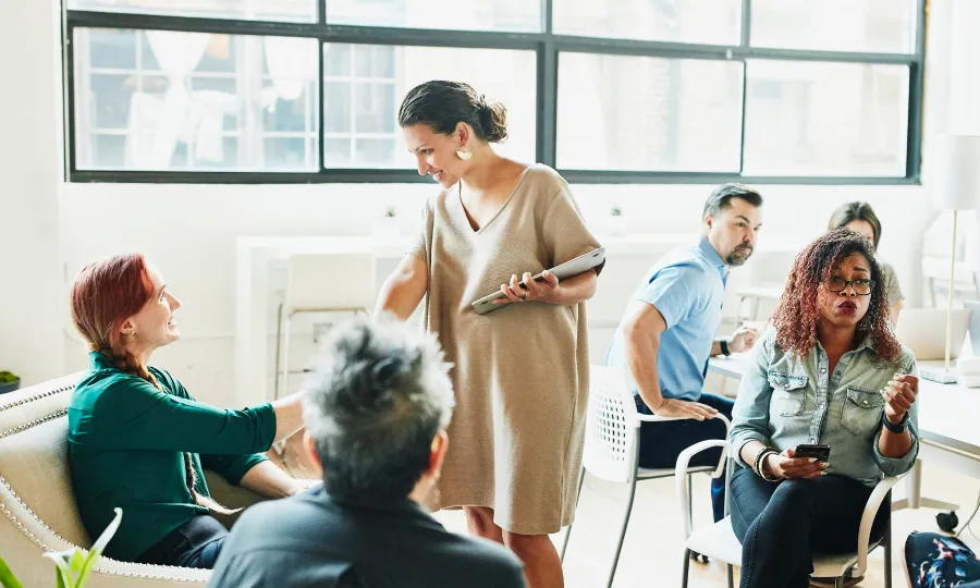 Colleagues in an open meeting space. One woman standing is shaking hands with a seated woman.