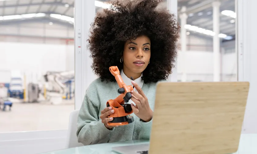 a person holding an engineering tool in front of a laptop.