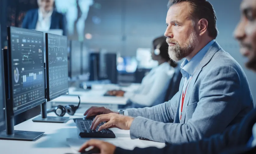 Man in an open plan office space looking at a computer monitor with graphs