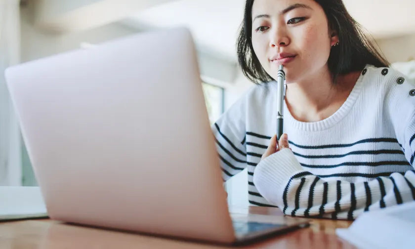 Thoughtful woman looking at laptop while holding a pen to her lips