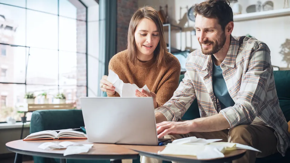 A man and woman working with financial data on a laptop at home