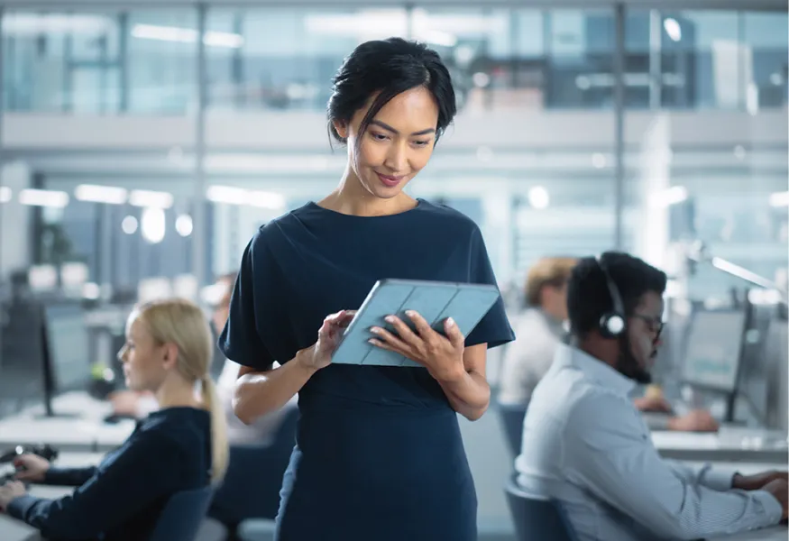 a woman holding a tablet surrounded by people working on computers