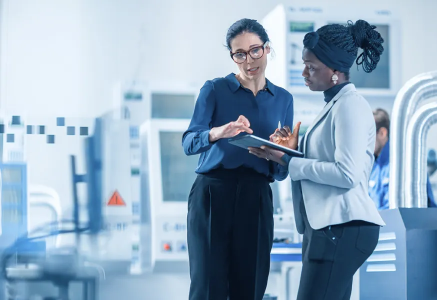 Two woman standing in a laboratory environment and discussing work on a digital tablet