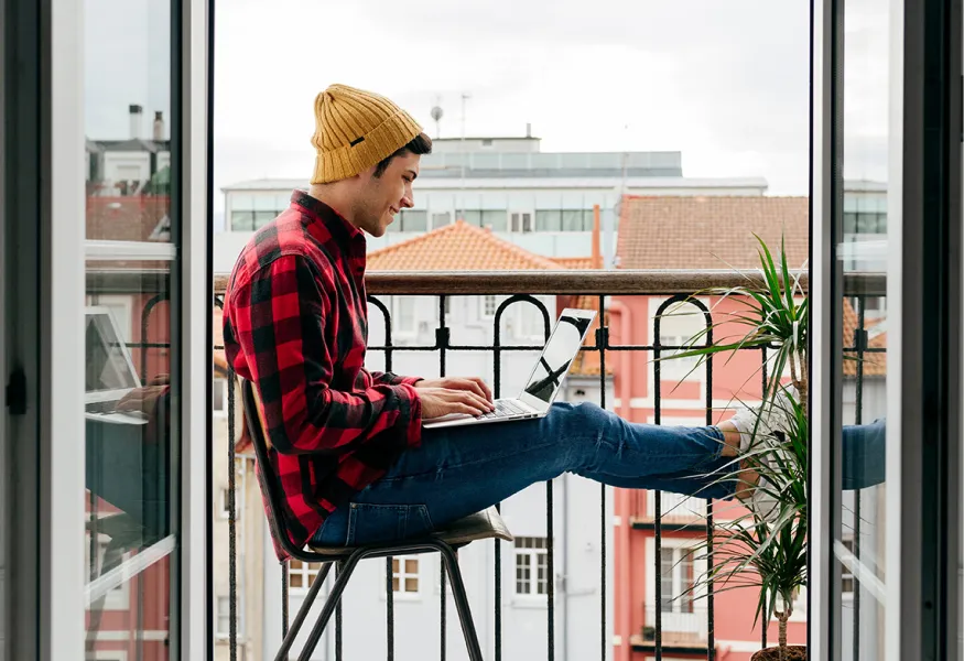 a man sitting at a table with a laptop on his balcony