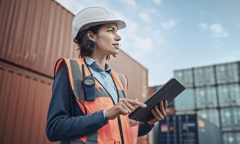 A woman wearing a hard hat and construction vest holding a tablet