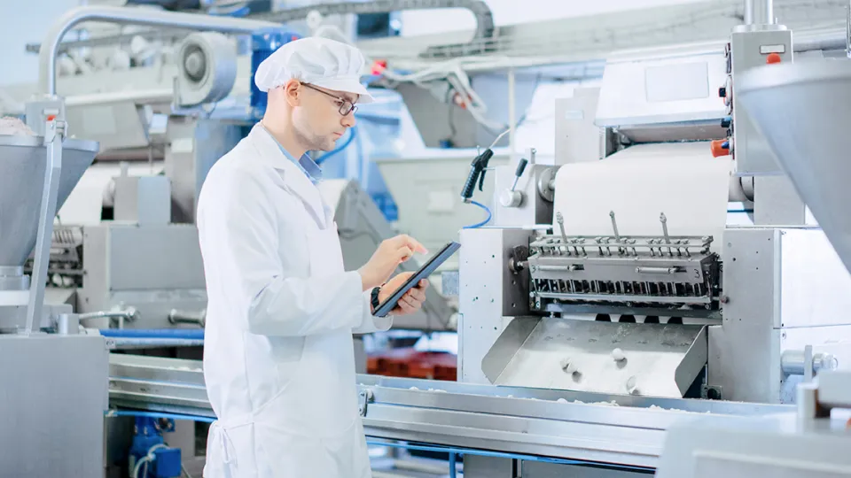 Man standing next to a factory machine and working on a digital tablet