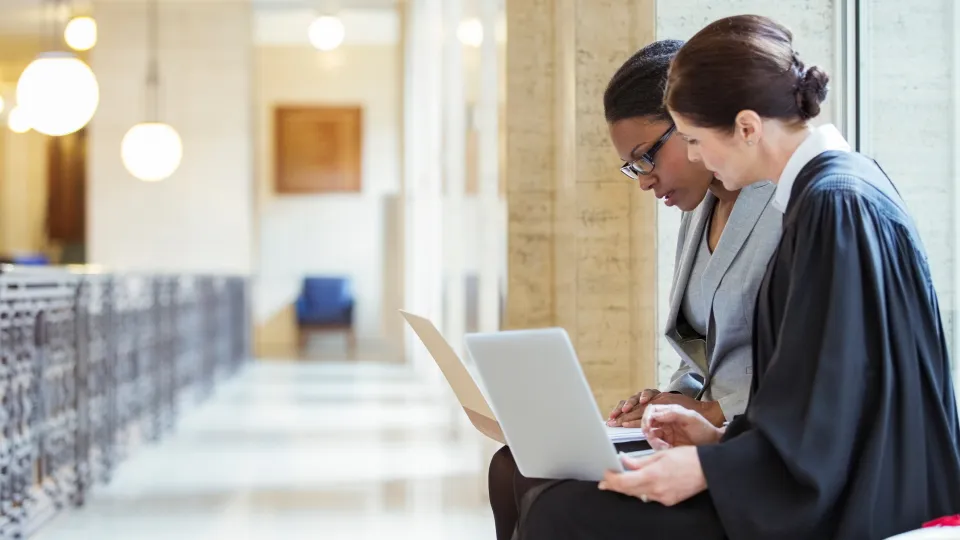 Two legal professionals working on laptops courthouse meeting space