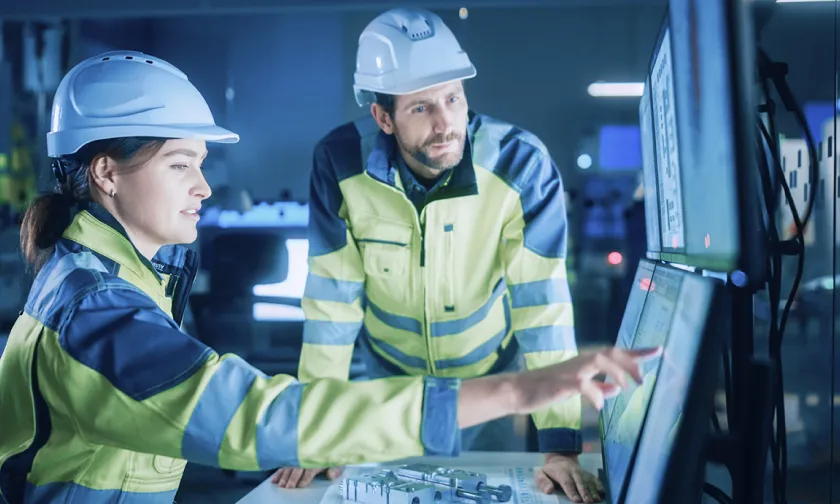 Man and woman looking a monitors while wearing safety gear