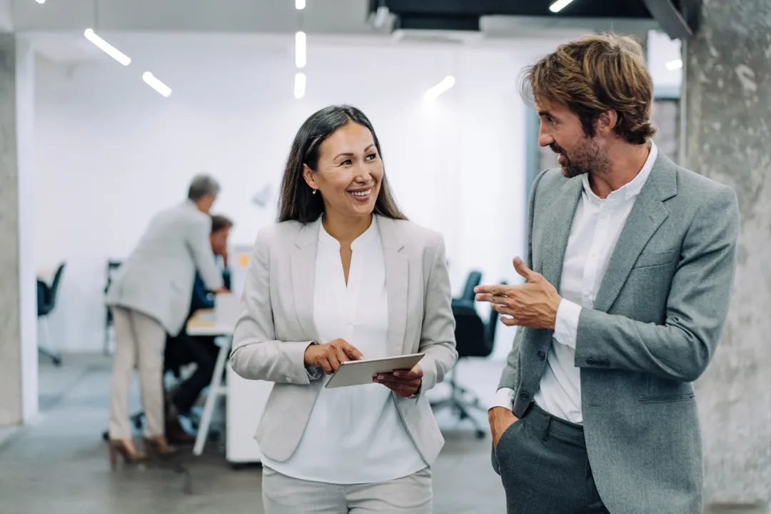 Business colleagues standing in an open office environment and discussing work on a digital tablet