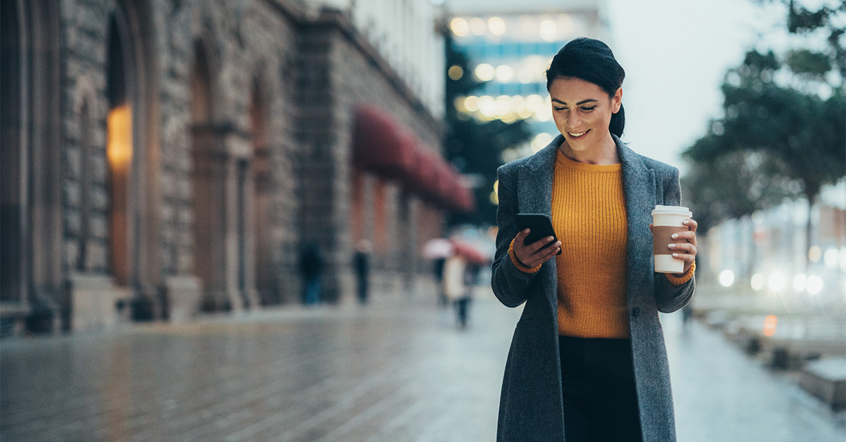 Women walking on the street looking down at phone in her hand.