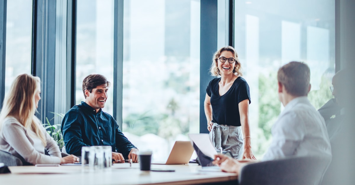 Smiling woman standing in a boardroom and interacting with seated people