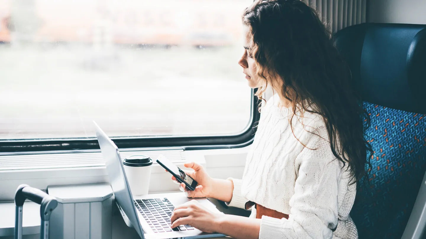 A woman using her phone and laptop on a train ride.