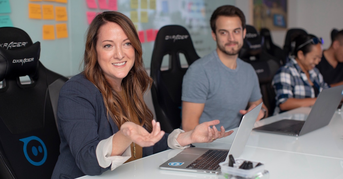 People sitting around office table with laptops.