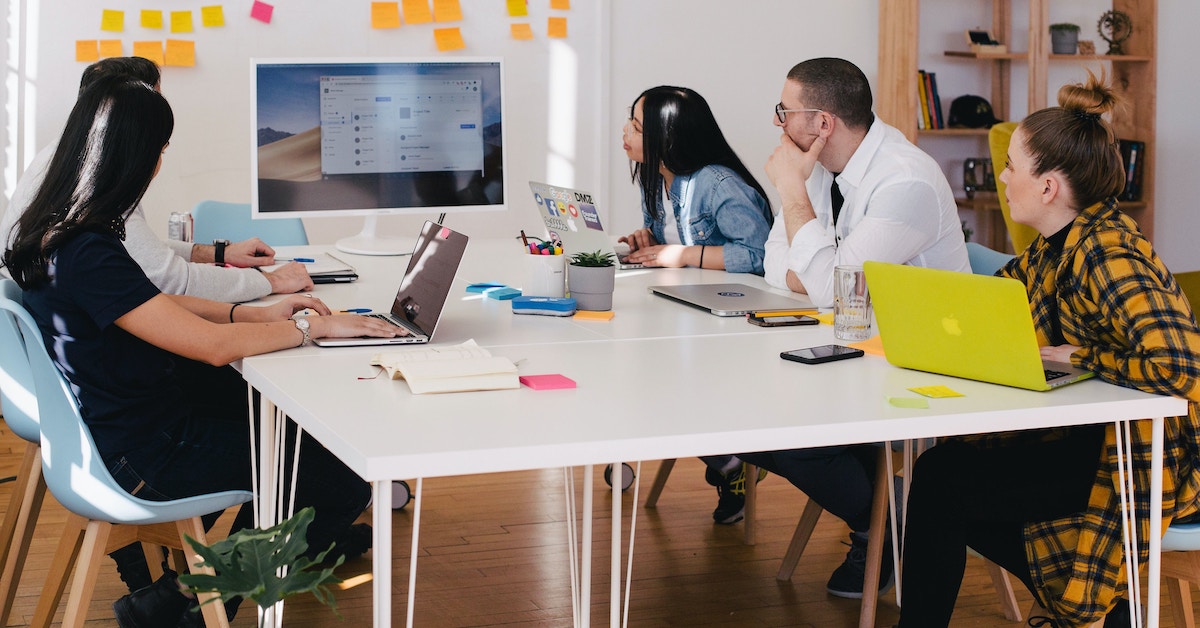 Five people sitting around an office table with laptops. 