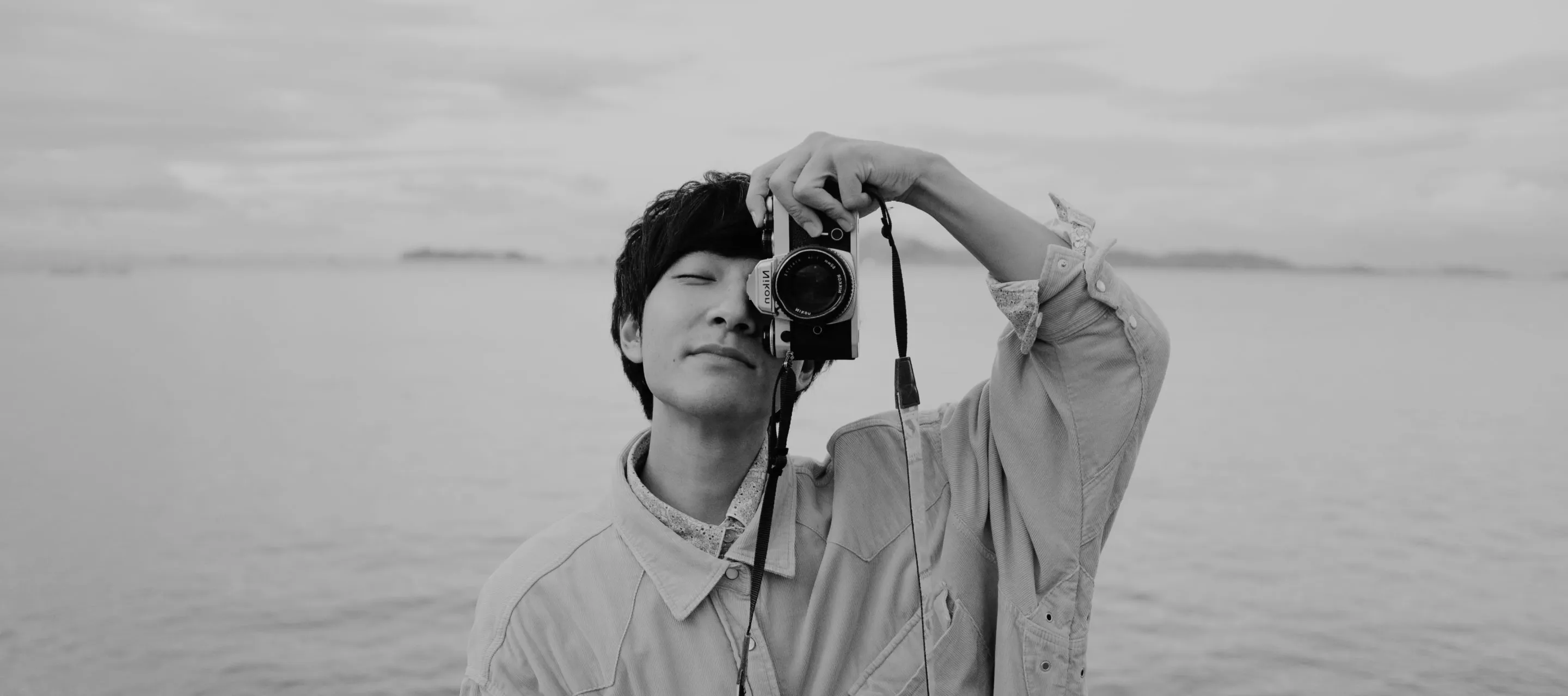 Black and white photo of a professional photographer holding a Nikon camera with one hand in front of his face