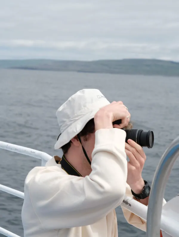 Photographer in a white bucket hat taking photos over the railing of a boat