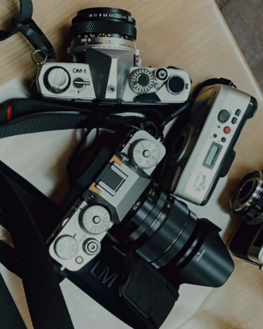 Tops of four digital cameras sitting on table including OM-1 and Yashica EZ Zoom digital gold camera