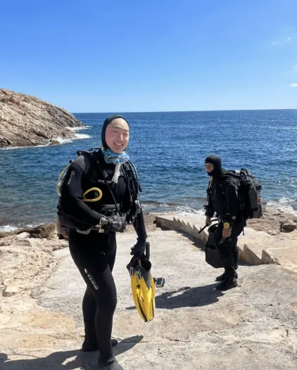 Two people in diving gear outside on rocks