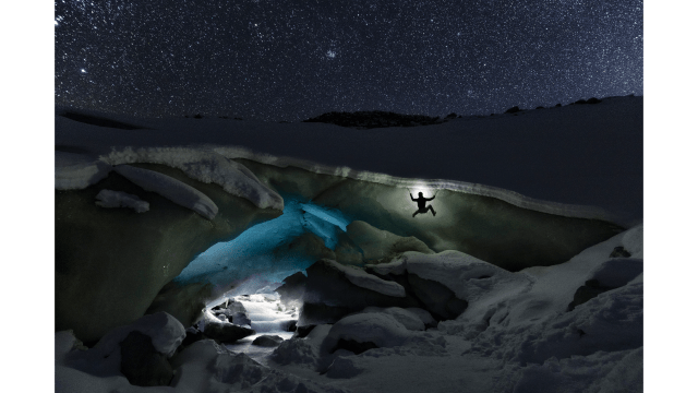 Ice climber on a glacier cave with head lamp, at night, in Switzerland.