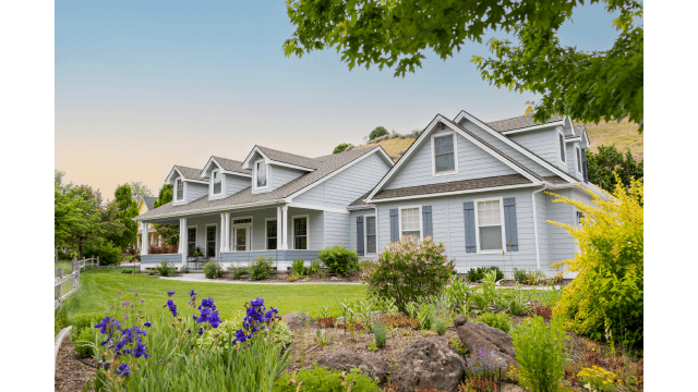 Large suburban home exterior at sunset with lawn and garden.