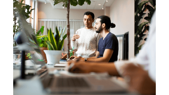 Two workers discuss in an office with plants.