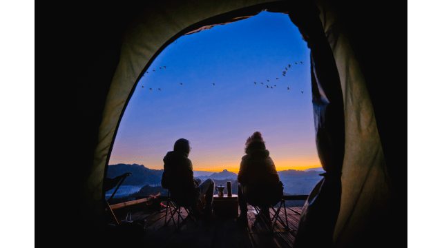 Two campers enjoy scenic views of mountain peaks in the morning.