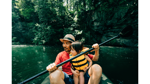 A father kayaks on a lake in a forest.