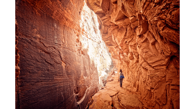 A female hiker walks through an open red cave or grotto.