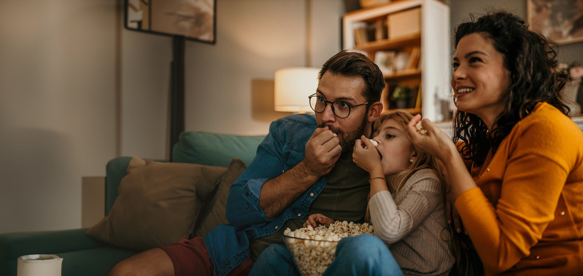 A family picture with a man, woman and two kinds sitting on a sofa iin the living room and watching home theatre