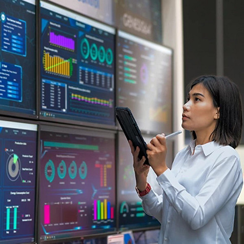 Lady standing facing six computer screens while using a tablet 