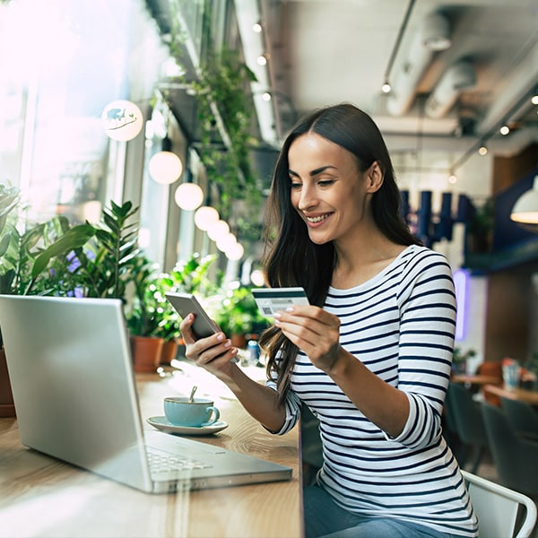 A woman siiting in front of her laptop with a smartphone in one hand and a card in the other