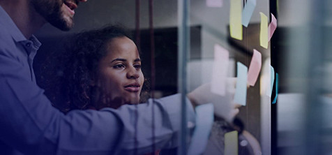 A man and woman sticking sticky notes to a glass wall.