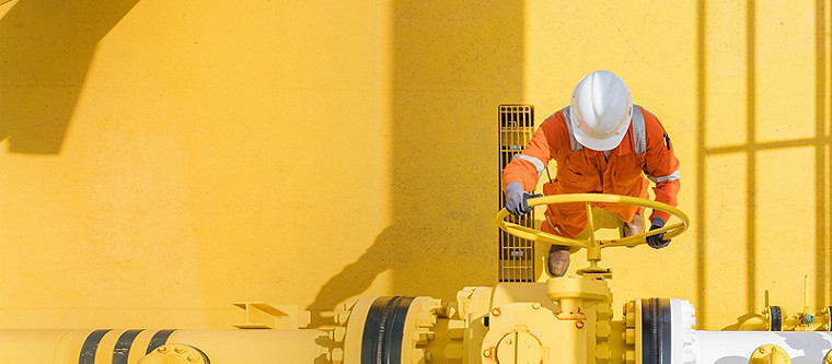 A worker in a high-visibility safety dress and white helmet operating a release valve